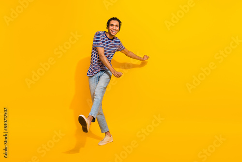 Full size photo of pleasant funky good mood man wear stripped t-shirt denim trousers go shopping isolated on yellow color background