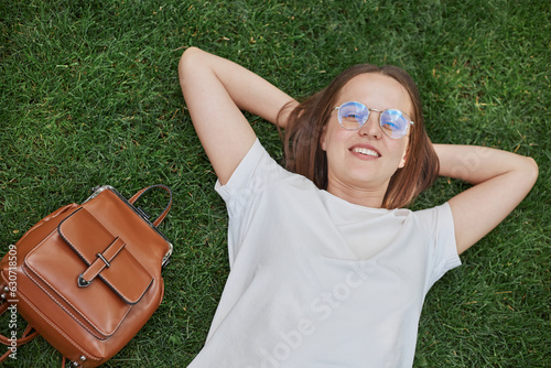 Smiling relaxing brunette woman lying down on grass with peace and tranquility wearing white T-shirt resting in nature smiling happily. photo