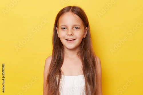Pleased pretty smiling happy little girl with ponytails standing isolated over yellow background looking at camera with positive expression.