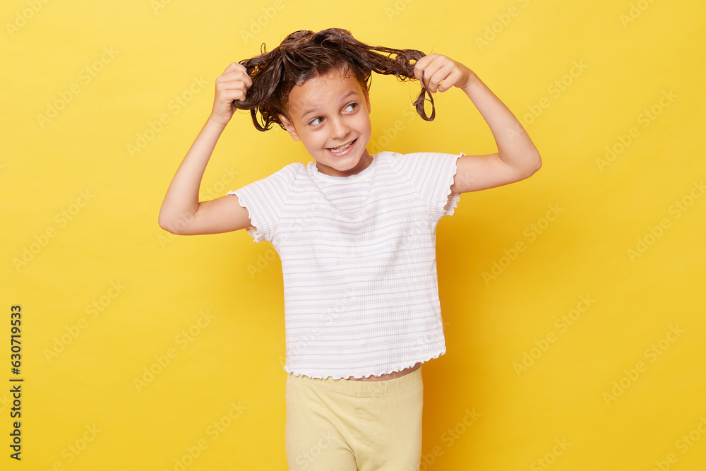 Little girl with wet hair wearing casual white T-shirt standing isolated over yellow background tangled hair while washing looking away with confused smile Little girl with wet hair wearing casual white T-shirt standing isolated over yellow background tangled hair while washing looking away with confused smile