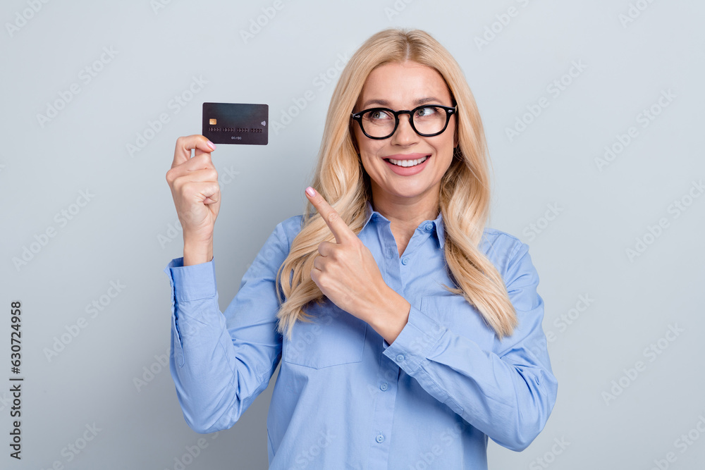 Photo of mature woman wear blue formal shirt indicate finger plastic card nfc atm payment bank account isolated on grey color background Photo of mature woman wear blue formal shirt indicate finger plastic card nfc atm payment bank account isolated on grey color background