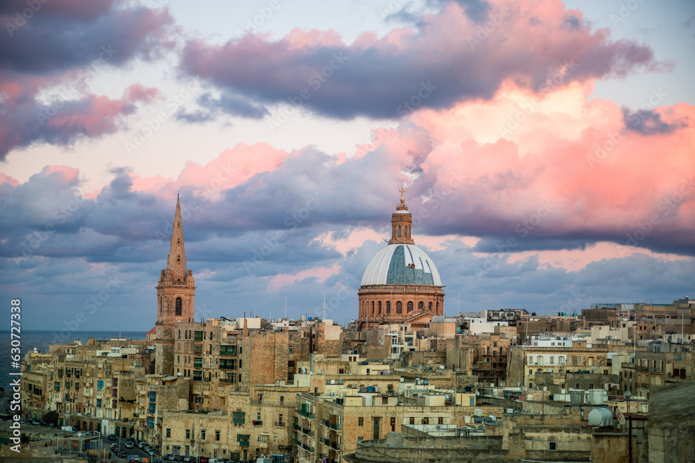 City view and skyline of Valletta at sunset. Historical buildings against blue sky and clouds colored by the sun