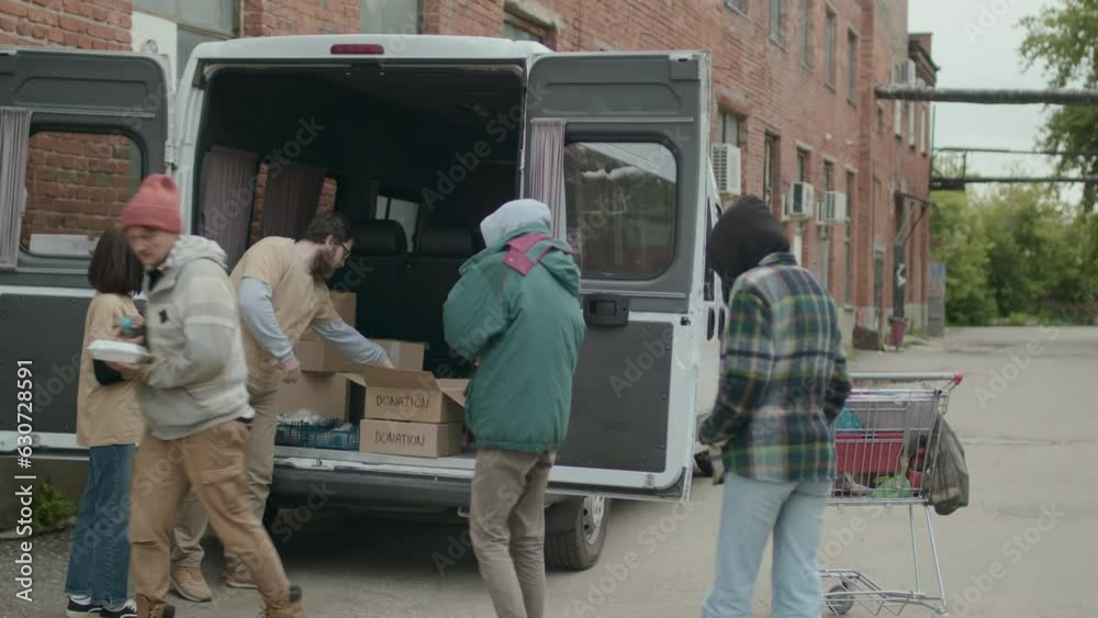 Long shot of volunteers giving free water and food for homeless people who standing in line to get supply in abandoned area