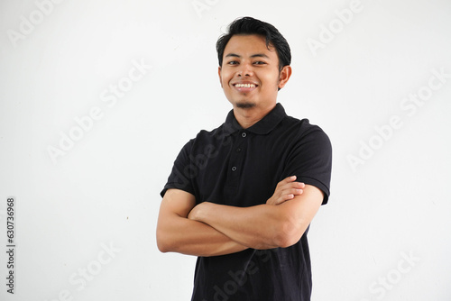 young asian man smiling happy at the camera with arms crossed wearing black polo t shirt isolated on white background
