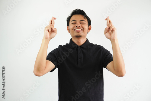 smiling Young handsome asian man isolated crossing fingers for having luck wearing black polo t shirt. photo