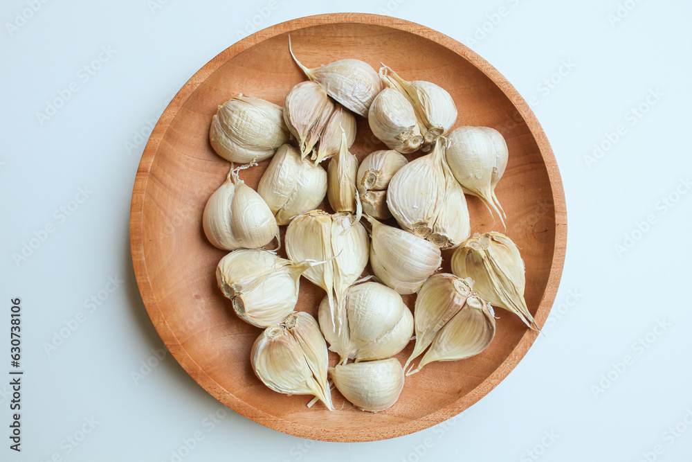 Garlic cloves or bulb on wooden plate, isolated on white background