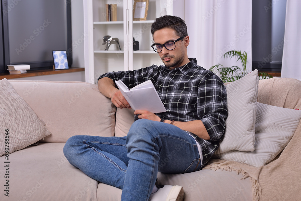 Cheerful bearded man in glasses immersed in a captivating book, savoring a serene moment in his cozy living room. Relaxation and literature concept for peaceful minds. Cheerful bearded man in glasses immersed in a captivating book, savoring a serene moment in his cozy living room. Relaxation and literature concept for peaceful minds.
