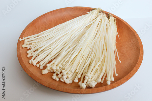 Enoki mushroom, or enokitake or Flammulina filiformis, on wooden plate, isolated on white background photo