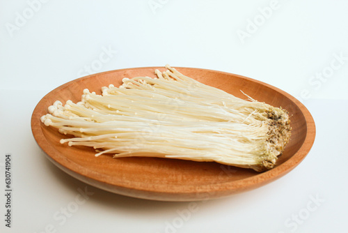 Enoki mushroom, or enokitake or Flammulina filiformis, on wooden plate, isolated on white background photo