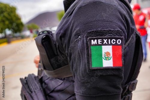 Closeup of the flag of Mexico on the arm of an uniformed Mexican guard, holding a rifle