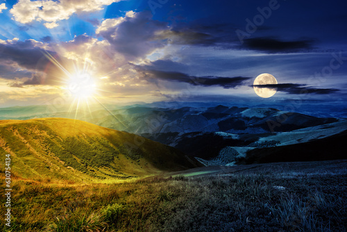 green grass on hillside meadow in high mountains under the cloudy blue sky with sun and moon at twilight. day and night time change concept. mysterious countryside scenery in morning light © Pellinni
