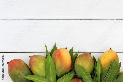 Exotic fruits,mangoes on green leaves, on white wooden table, background, top view, place for text photo