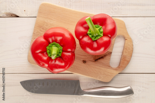 Two sweet red peppers with wooden kitchen board and knife on wooden table, macro, top view.