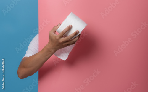 Male hand holding white toilet paper roll on blue background,copy space for text