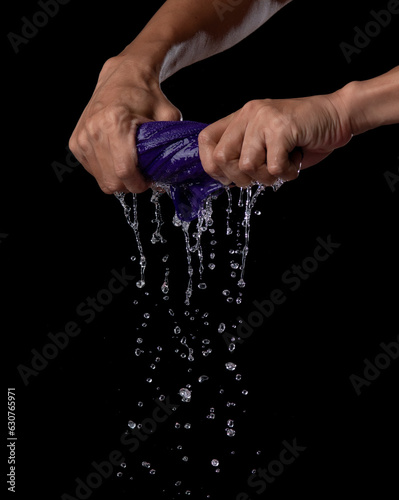 Two hands wring wet cloth after washing by twist and squeeze over dark background