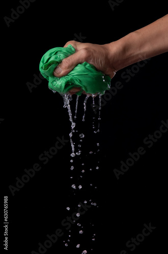 Two hands wring wet cloth after washing by twist and squeeze over dark background