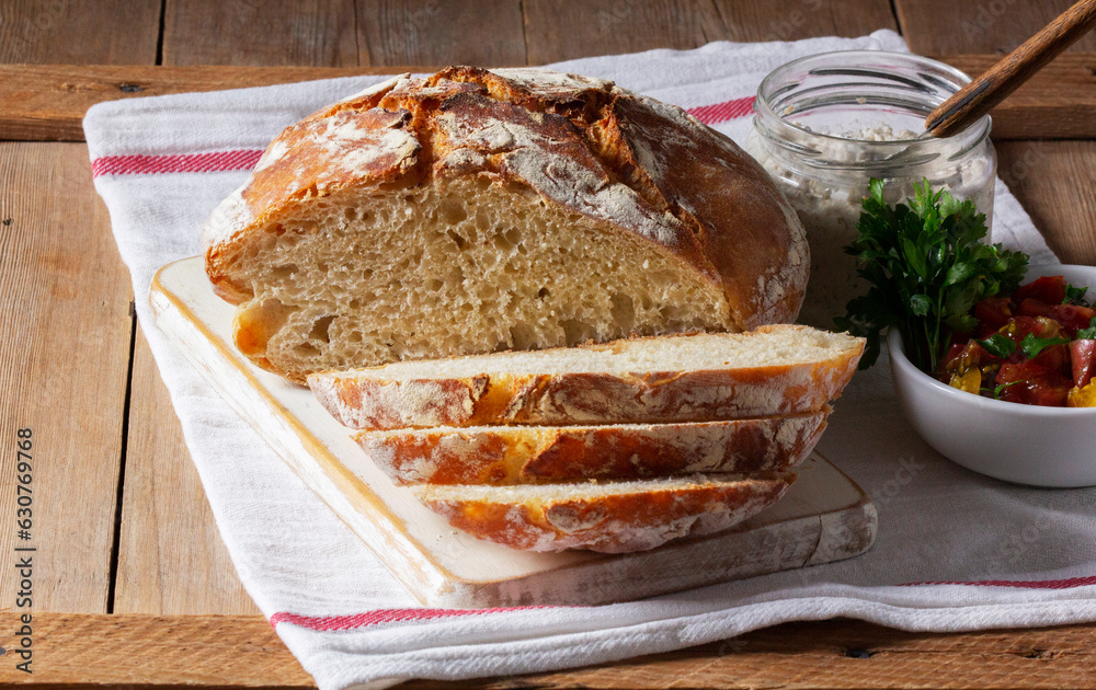 Round yeast bread made from white and whole grain flour, tomato salad and pate on a wooden background. Rustic style.