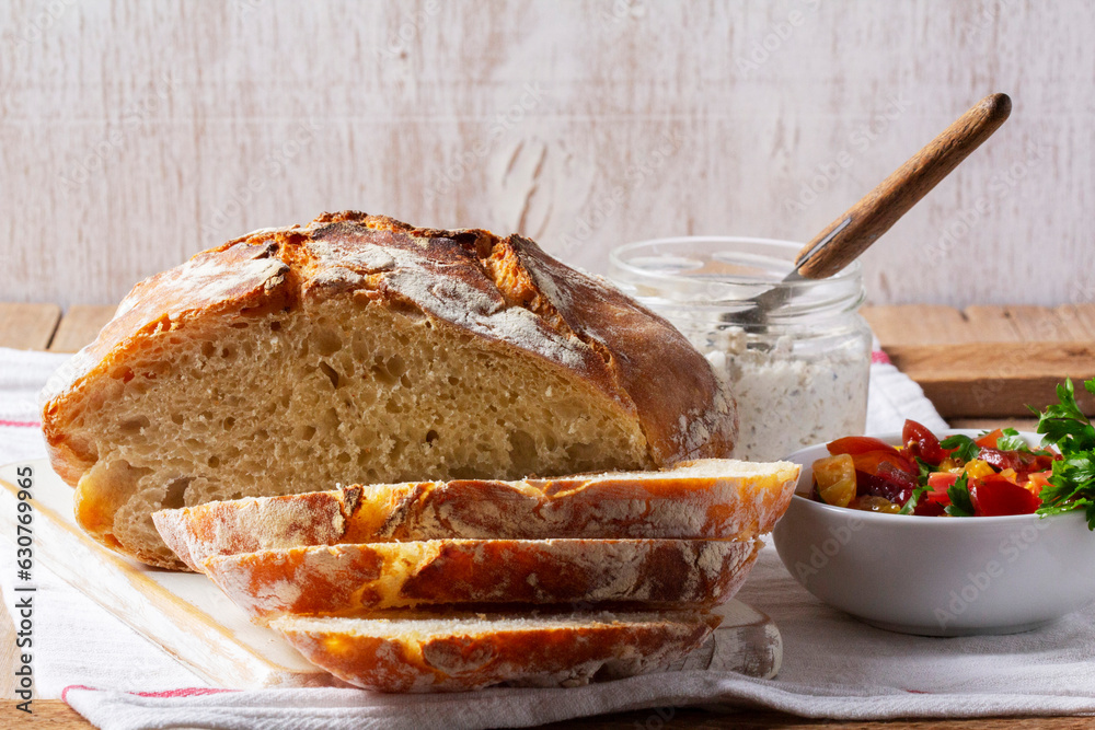 Round yeast bread made from white and whole grain flour, tomato salad and pate on a wooden background. Rustic style.