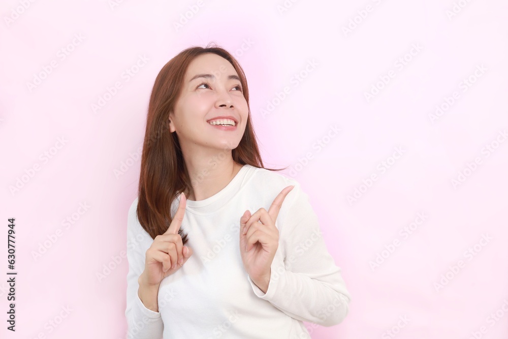 Smiling Asian woman standing over isolated pink background and pointing finger by the side to copy space. Smiling Asian woman standing over isolated pink background and pointing finger by the side to copy space.