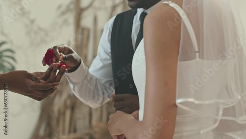 Cropped shot of unrecognizable Black marrying couple exchanging wedding rings during ceremony indoors