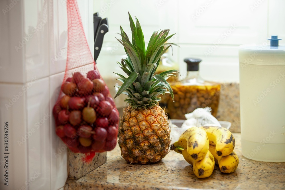 Countertop with yellow pineapple and a bunch of ripe yellow bananas on the side in a kitchen setting Countertop with yellow pineapple and a bunch of ripe yellow bananas on the side in a kitchen setting