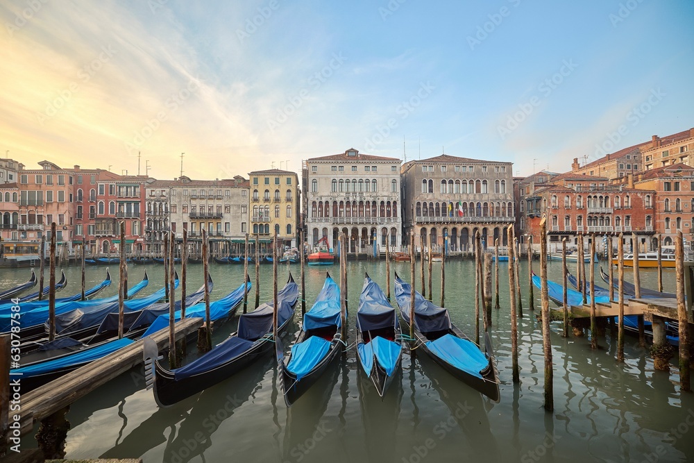 Naklejka premium Picturesque scene of gondolas on canal in Venice, Italy, surrounded by urban buildings at sunset