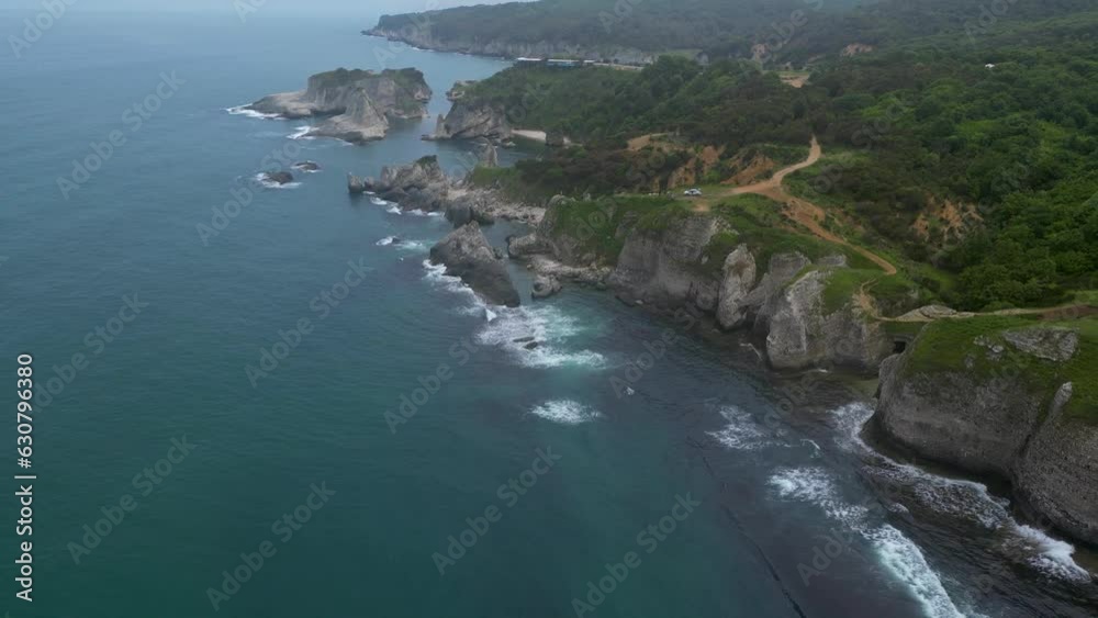 Aerial of the calm sea waves hitting the rocky shore and the cliffs under the blue sky Aerial of the calm sea waves hitting the rocky shore and the cliffs under the blue sky