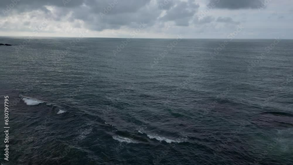 Aerial of a person standing on the edge of a cliff and looking at the calm sea