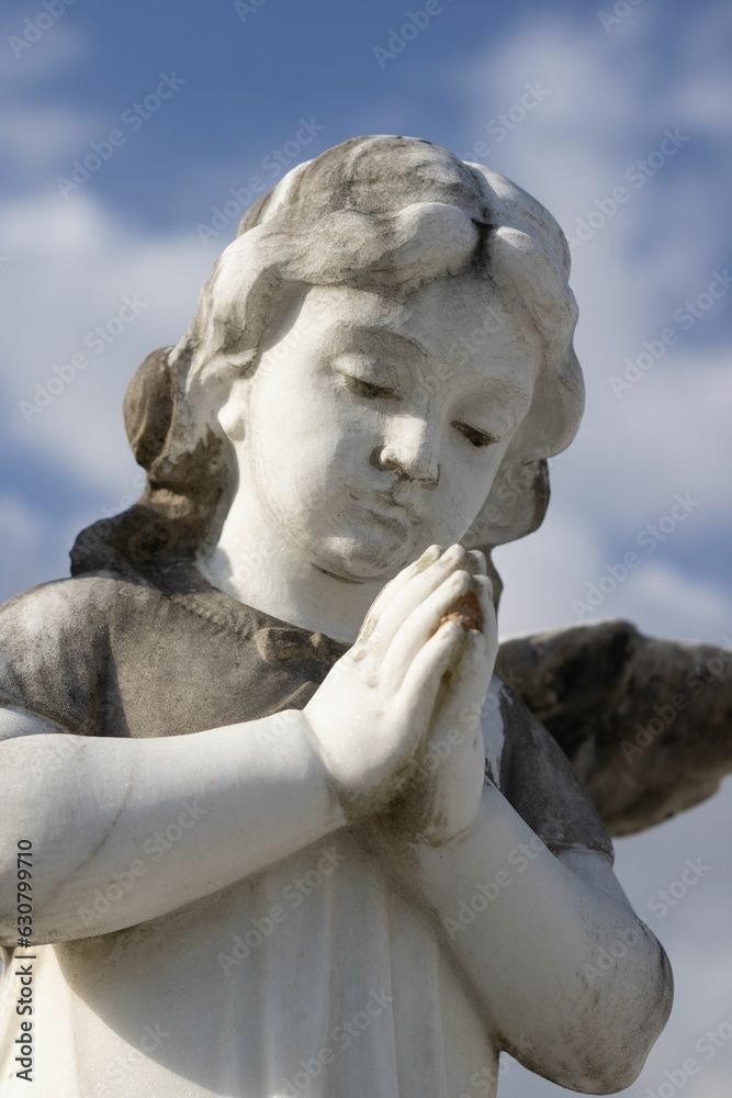 Bronze sculpture of a figure in a contemplative pose against a cloudy blue sky