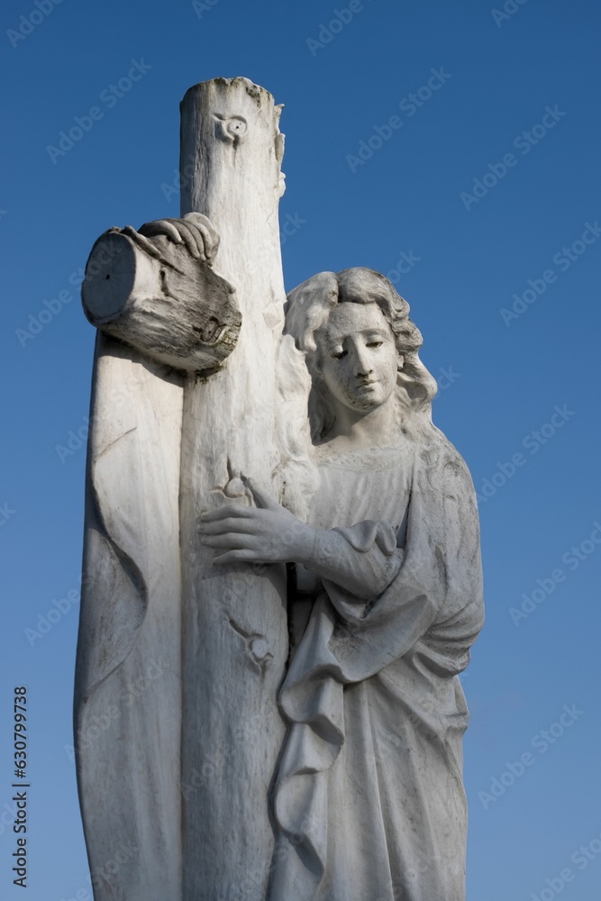 Angelic figure stands against a serene sky as they hold a cross in their hands
