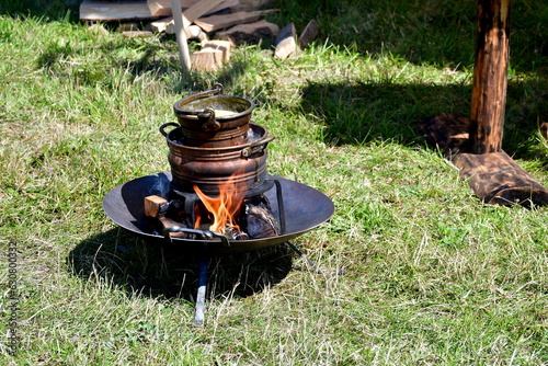 A close up on a wooden or clay pot standing on a fire pit used to melt some bee wax in order to make handmade candles and decorations seen during a medieval fair on a Polish countryside