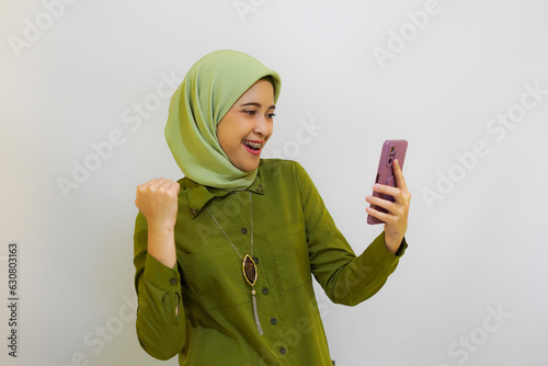 Happy Young Asian woman holding her phone for advertising concept. Green outfit hijab woman concept photo