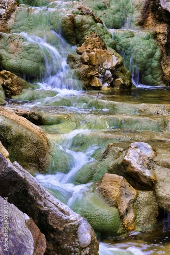 Serene river with vibrant green algae around its rocks and boulders, Tuscany, Italy
