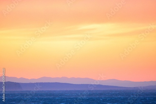 Scenic view of a stunning sunset over the ocean, with colorful mountains in the background