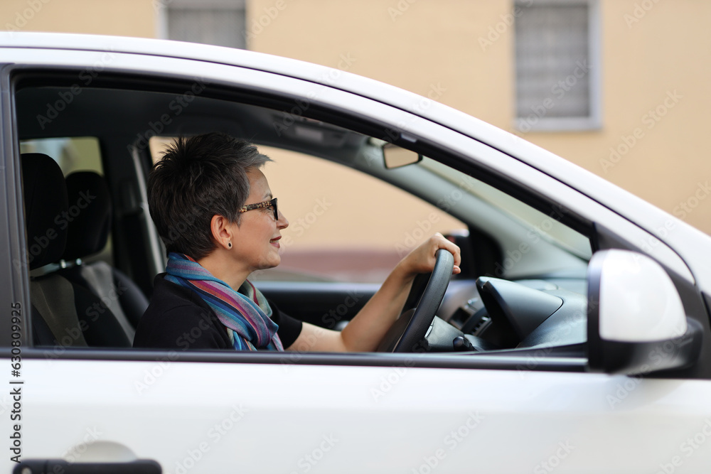 A mature business woman drives a car in the city, wearing a scarf to prevent infection. He pays attention to the road and the traffic, avoiding accidents and contamination.