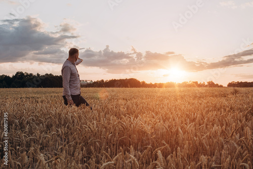Wheat field at sunset. Agriculture concept, a farmer in the field checks the quality of the crop. Front view © Olha