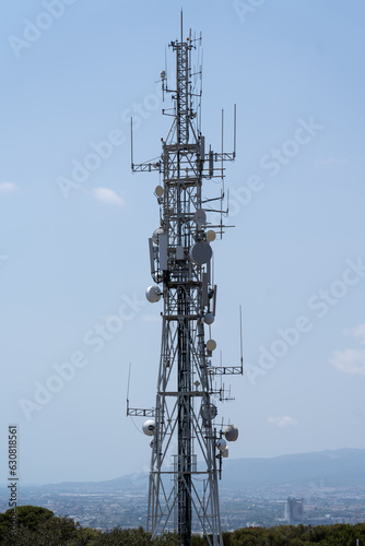 Big tower with antennas and satellites in front of the mountains and the city of Barcelona, no people and clear sky