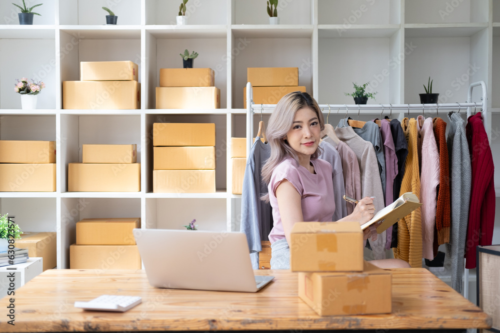 Young woman owner ship business start small business in a cardboard box and calculate price product by calculator and laptop computer Young woman owner ship business start small business in a cardboard box and calculate price product by calculator and laptop computer
