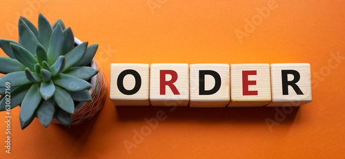 Order symbol. Wooden cubes with word Order. Beautiful orange background with succulent plant. Business and Order concept. Copy space.