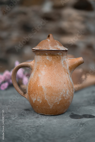 Pichet ancien rustique en céramique artisanale posé sur une table de campagne et entouré de fleurs