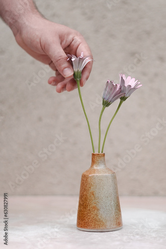 Vase soliflore décoratif en céramique artisanale, avec un petit bouquet de fleurs et une main tendue sur un fond neutre