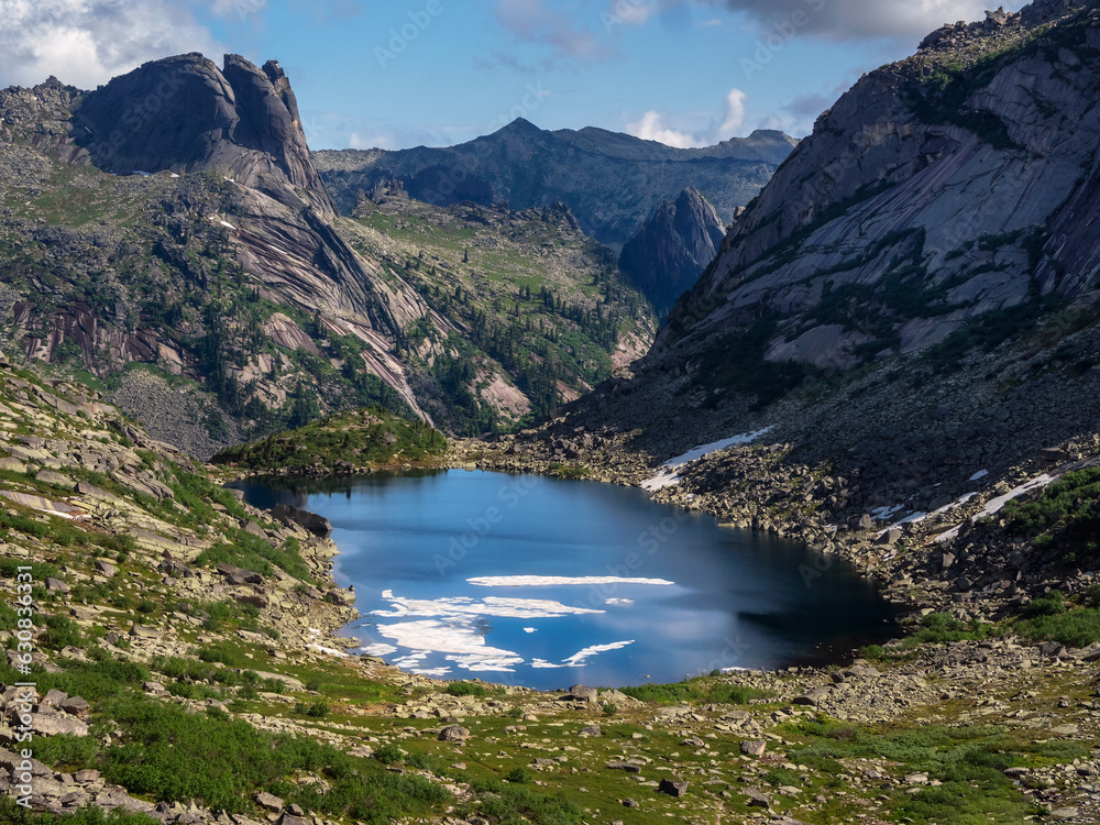 Awesome alpine landscape with mountain lake in stone green valley under blue sky. Atmospheric highland scenery with beautiful glacial lake among sunlit hills and rocks against mountain range. Awesome alpine landscape with mountain lake in stone green valley under blue sky. Atmospheric highland scenery with beautiful glacial lake among sunlit hills and rocks against mountain range.