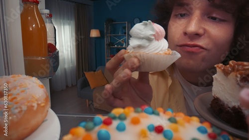 Portrait of a man at an open refrigerator filled with various dessertsclose up. The man holds a cupcake in his hand, fixing on him a greedy, insatiable look. View from inside the refrigerator.