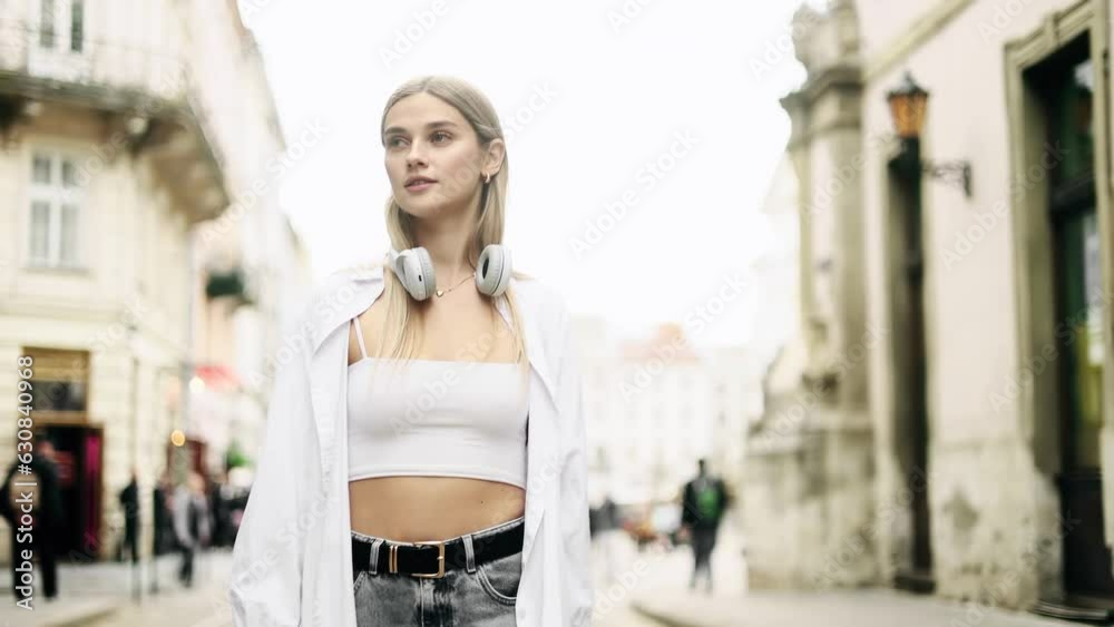 Charming young blond woman walking down the street with flying hair and looking around outdoors Happy relaxed lady walking on the city centre enjoying beautiful day alone Charming young blond woman walking down the street with flying hair and looking around outdoors Happy relaxed lady walking on the city centre enjoying beautiful day alone