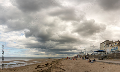 Langrune-Sur-Mer, France - 07 19 2023: View of a cloudy rainy sky, the seawall, beach cabins and people above the sea from the beach.