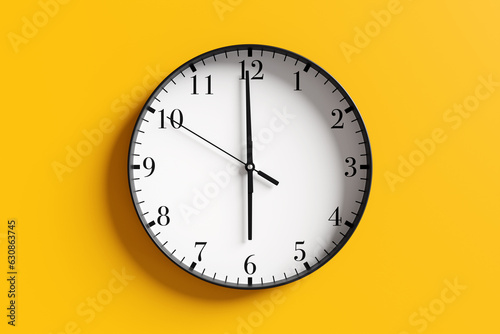 Round black and white wall clock at almost 6 o'clock on yellow background. Illustration of the concept of wake up time and off duty time photo