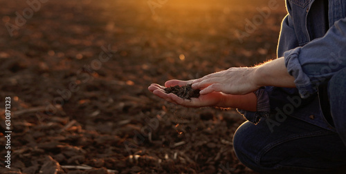 Male farmer's hand holds a handful of dry ground and checks soil fertility and quality before sowing crops on plowed field at sunset. Cultivated land. Concept of organic agriculture and agribusiness.