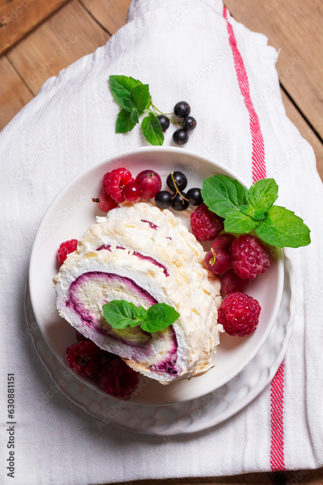 Meringue roll with whipped cream and currant curd, served with berries on a ceramic plate. Rustic style.