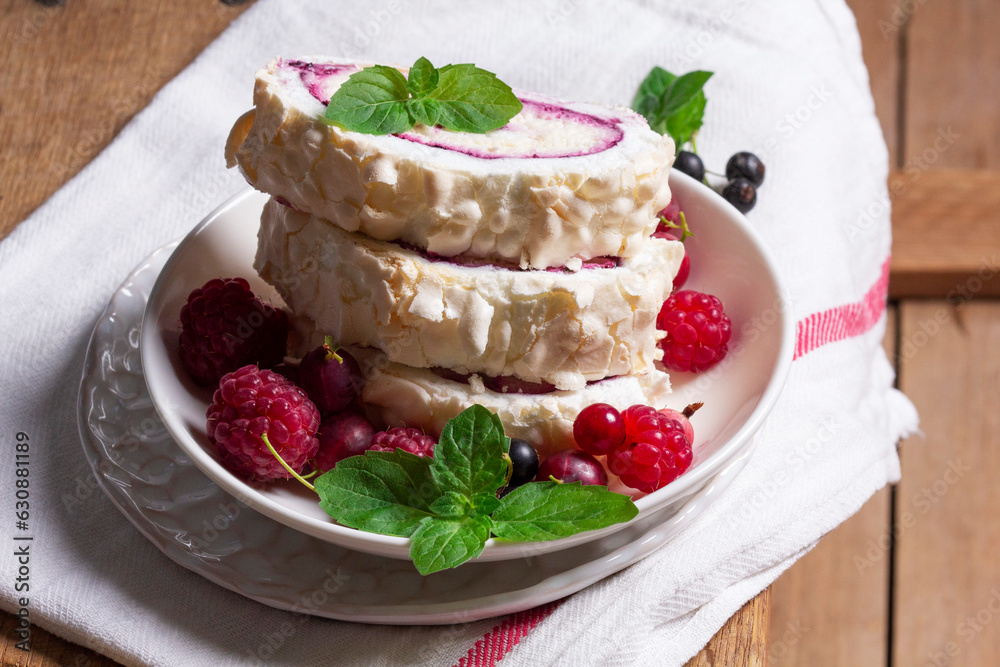 Meringue roll with whipped cream and currant curd, served with berries on a ceramic plate. Rustic style.