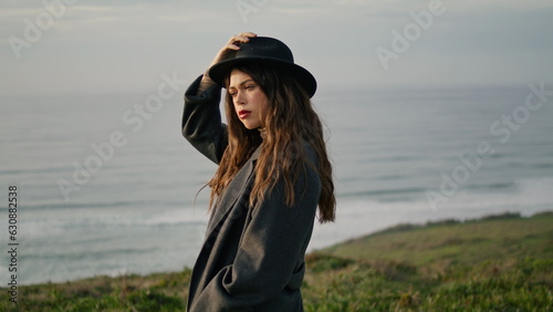 Model posing holding hat at ocean coast gloomy evening close up. Serious woman